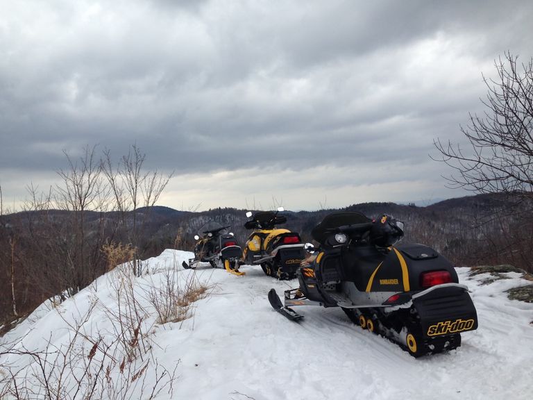 Parked snowmobiles on a trail with view of the mountains